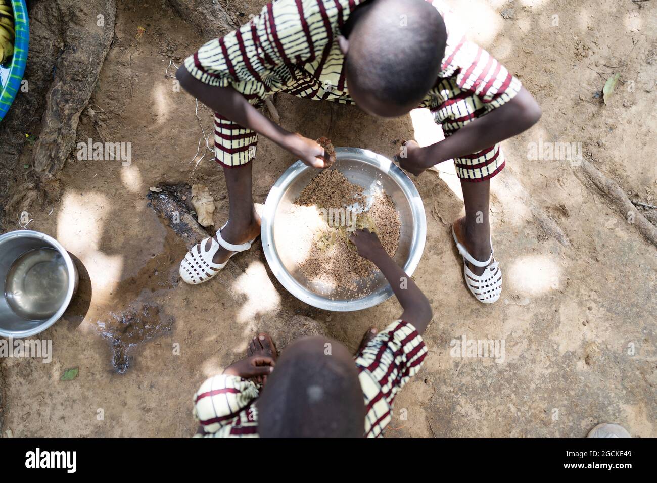 In diesem Bild teilen sich zwei kleine schwarze afrikanische Brüder in identischer Kleidung einen fleischlosen Reisteller, der auf dem Boden sitzt, mit ihrem rechten han Stockfoto