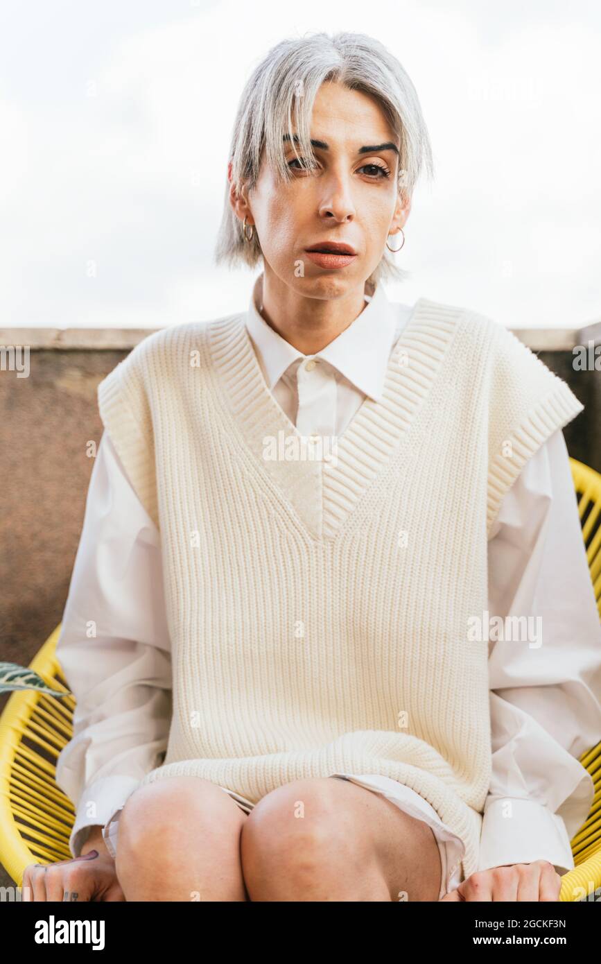 Stilvolle TransgenderFrau in trendigem Outfit sitzt im Sessel auf der