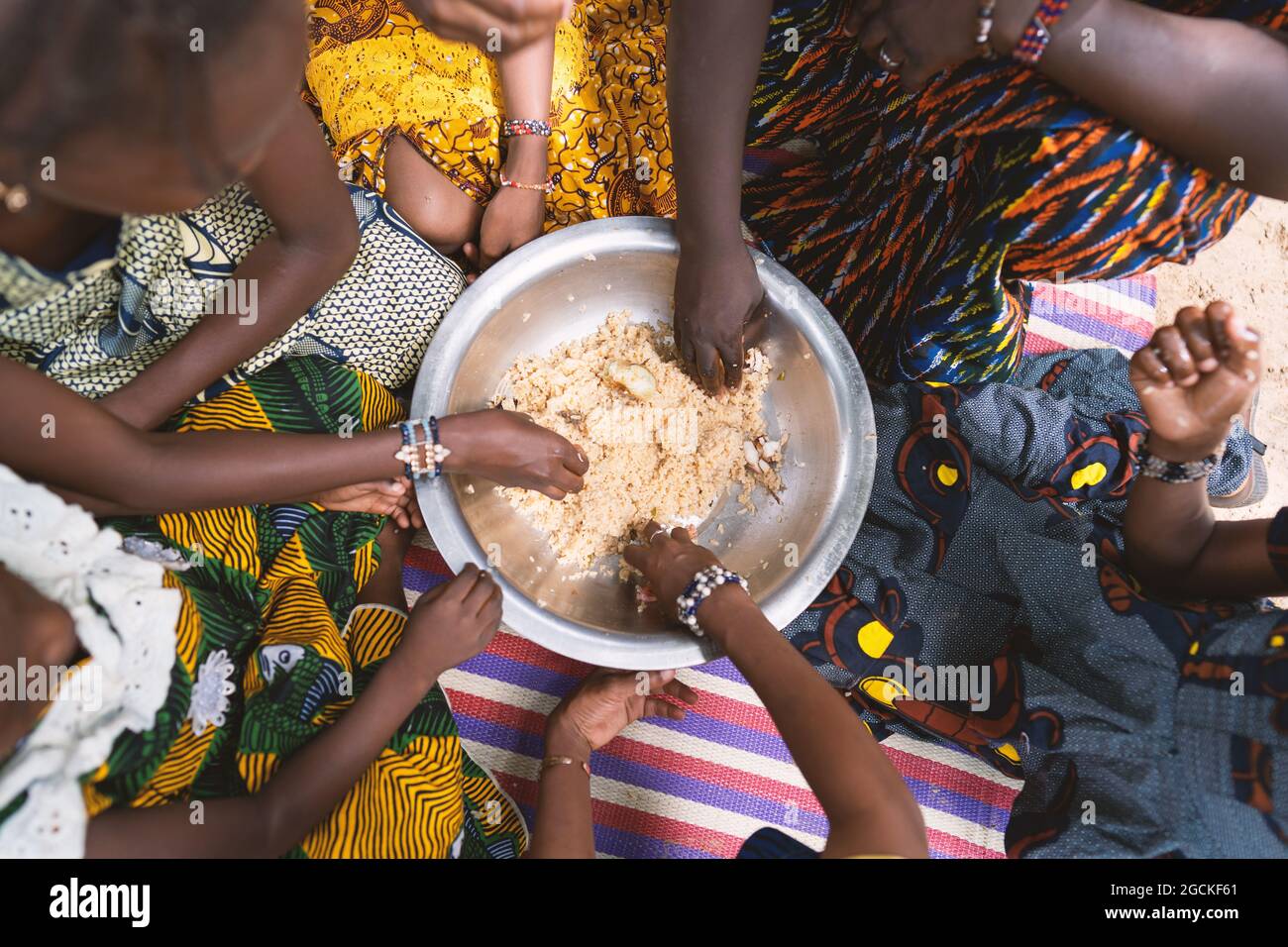 In diesem Bild sitzt eine Gruppe schwarzafrikanischer Mädchen im Kreis um einen großen Teller Getreide und isst zusammen mit dem ihre magere vegane Mahlzeit Stockfoto