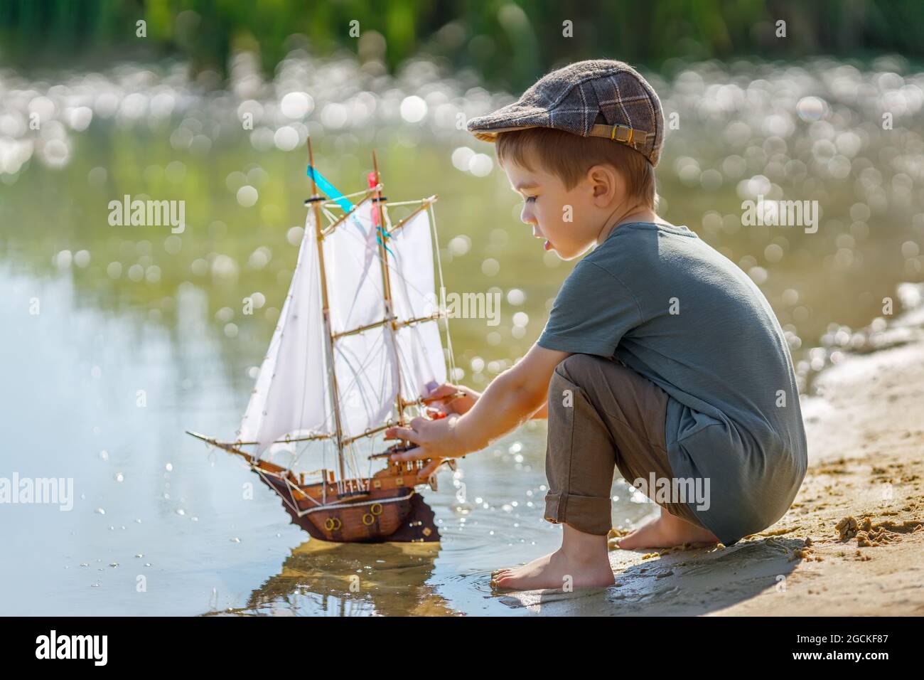 Kleiner Junge in Kappe, der Schiff auf dem Fluss ablauncht Stockfoto