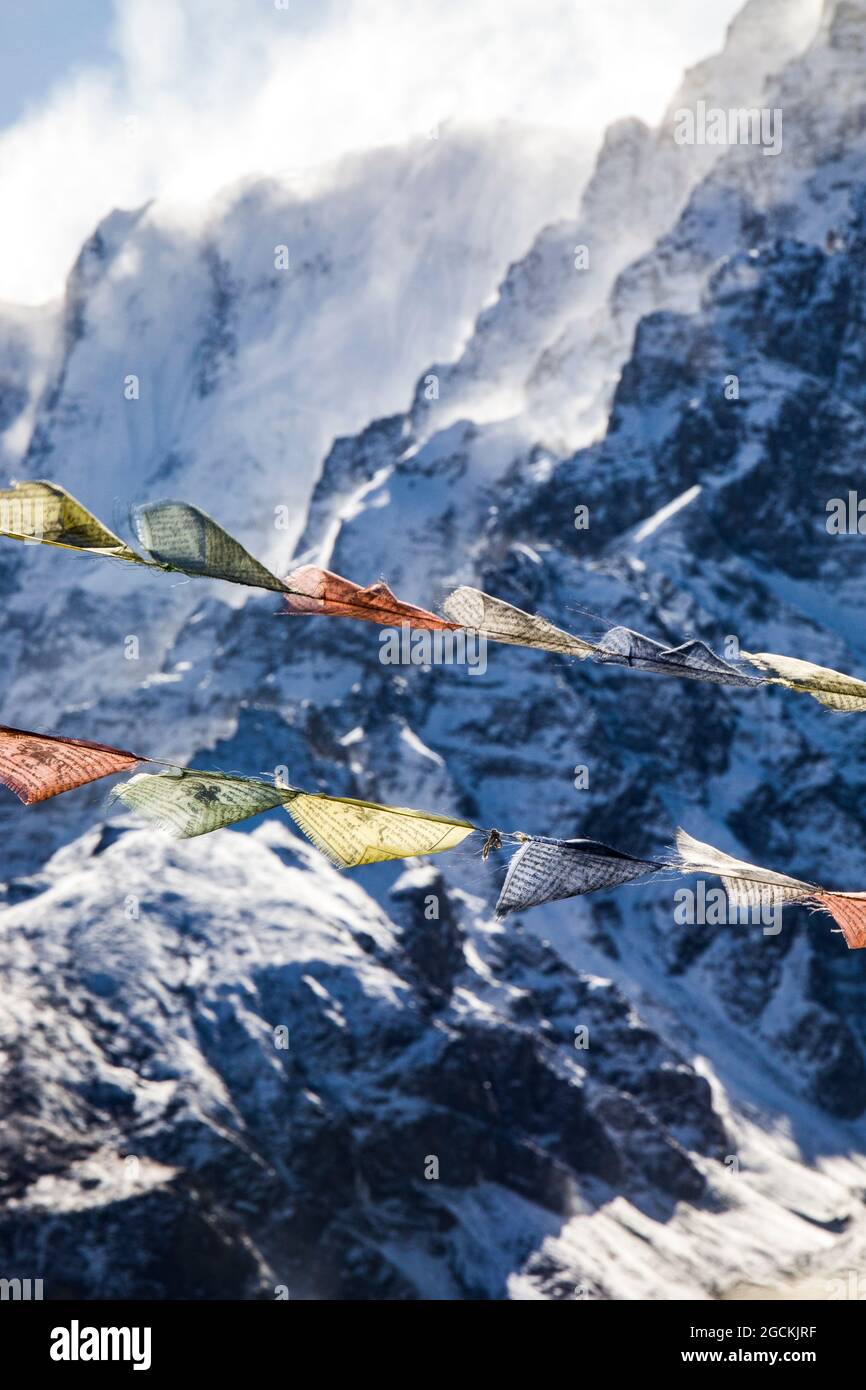 Reihen von bunten buddhistischen Gebetsfahnen, die im Winter in Nepal auf dem Hintergrund des felsigen Himalaya mit Schnee bedeckt sind, an Seilen hängen Stockfoto