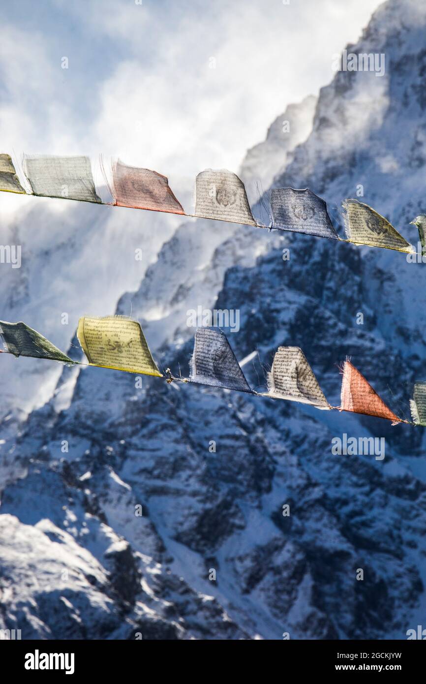 Reihen von bunten buddhistischen Gebetsfahnen, die im Winter in Nepal auf dem Hintergrund des felsigen Himalaya mit Schnee bedeckt sind, an Seilen hängen Stockfoto
