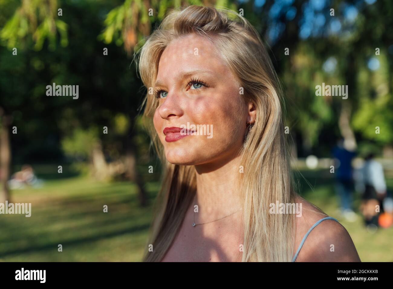 Glückliche Hündin mit blonden Haaren und Schatten im Gesicht, die am sonnigen Tag im Sommerpark steht und wegschaut Stockfoto