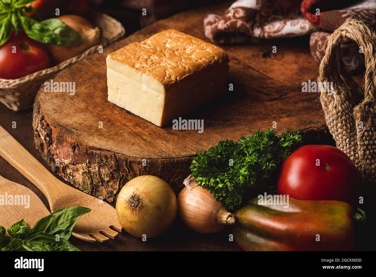 Halbweichen Käse zwischen frischen Tomaten und Zwiebeln auf dem Tisch mit Spatel und lockiger Petersilie schneiden Stockfoto