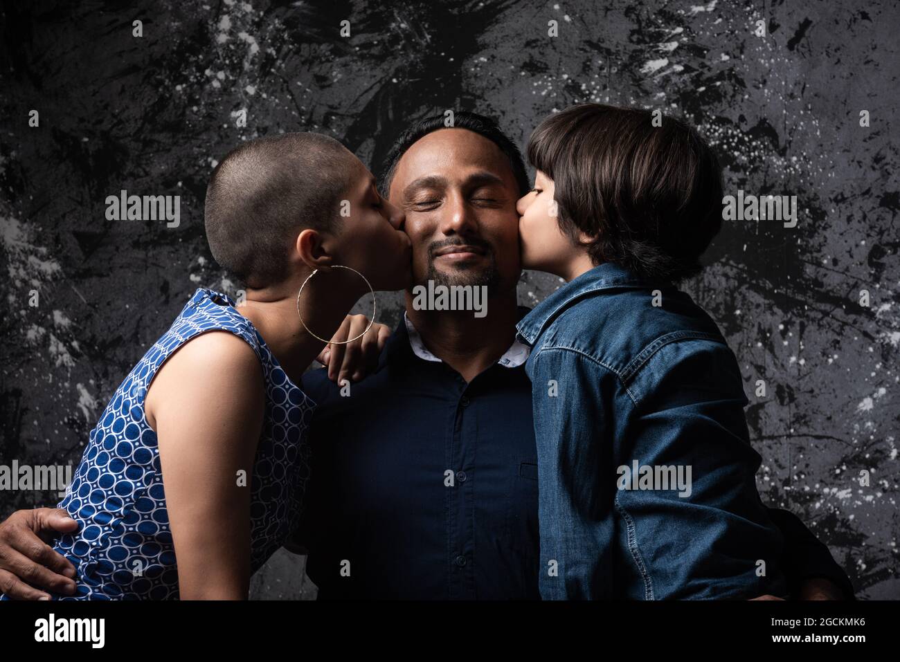 Multiethnisch liebende Frau und Teenager-Sohn küssen Mann auf Wange auf dunklem Hintergrund im Studio Stockfoto