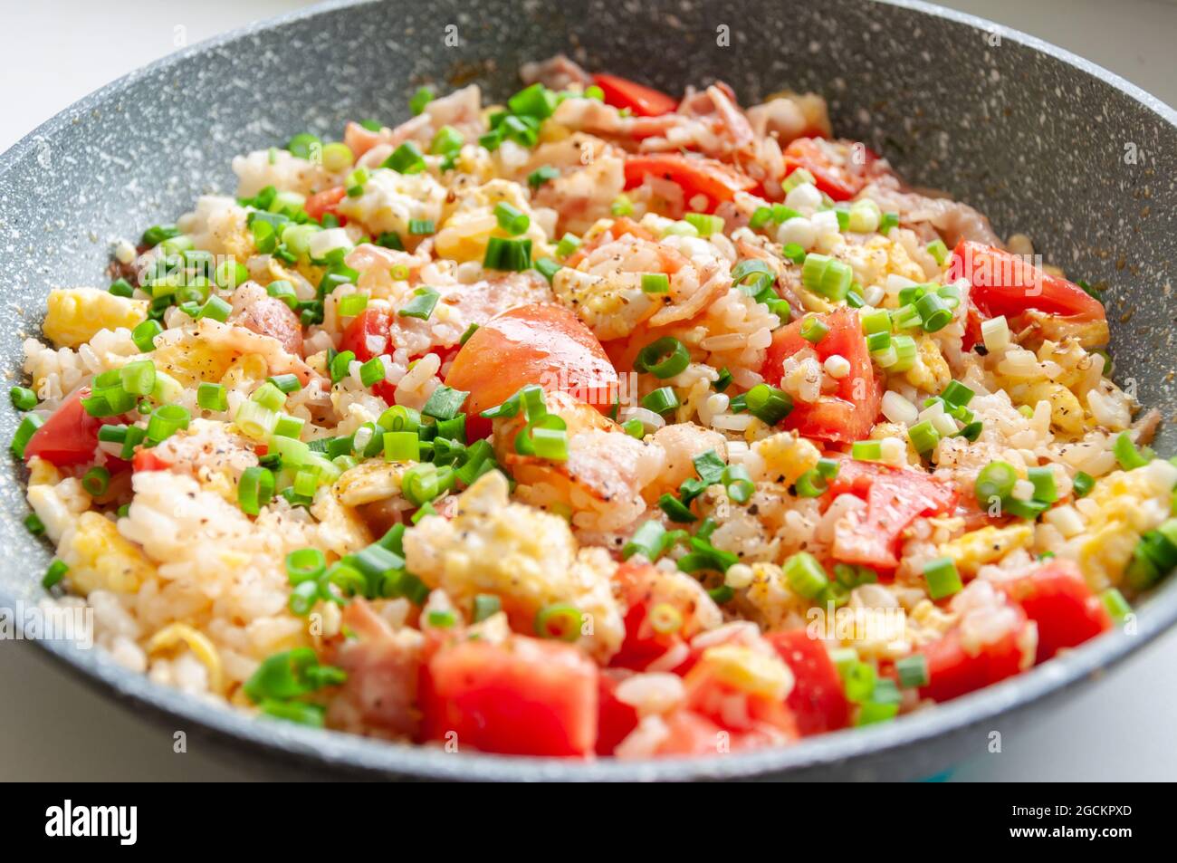 Gebratenen Reis in der Pfanne umrühren. Leckerer Reis, der mit Gemüse und Speck in einer Pfanne auf dem Tisch zubereitet wird. Stockfoto