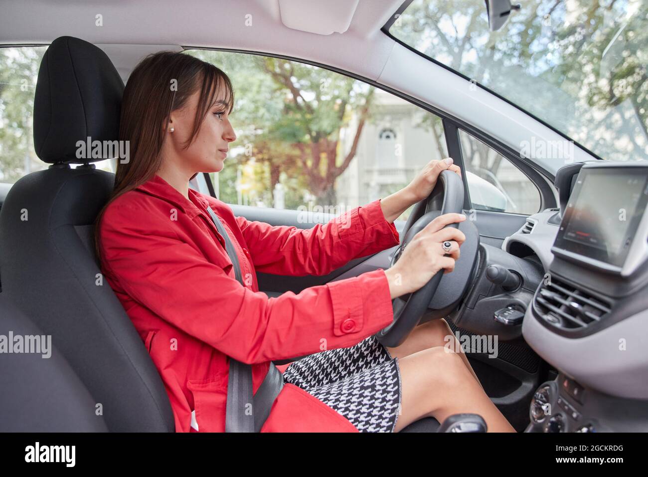 Durch das Fenster Seitenansicht der selbstbewussten jungen Frau in roter Jacke fahren moderne Automobil in der Stadt Stockfoto