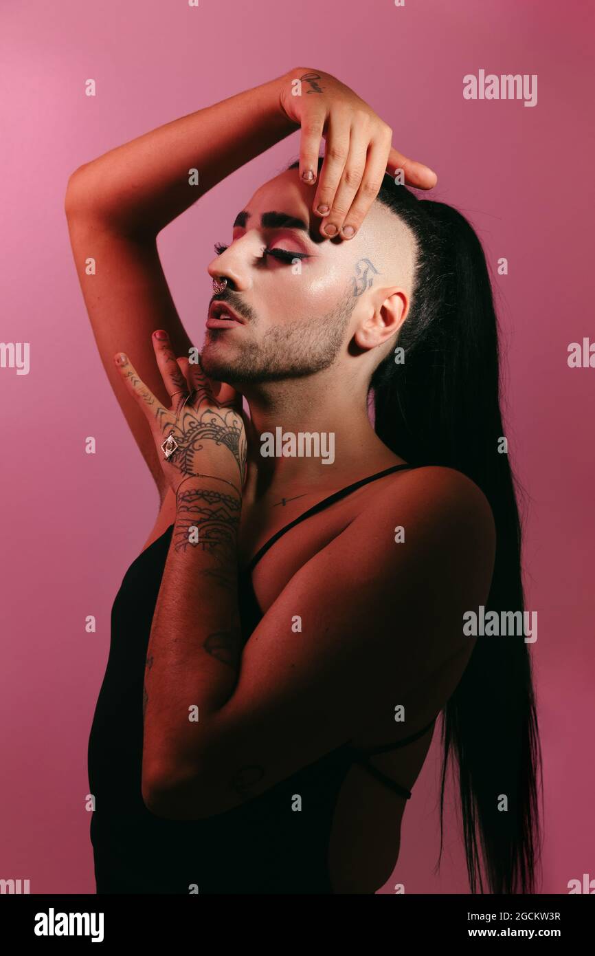 Seitenansicht Porträt der glamourösen Transgender bärtigen Frau in raffiniertem Make-up posiert mit geschlossenen Augen vor rosa Hintergrund im Studio Stockfoto