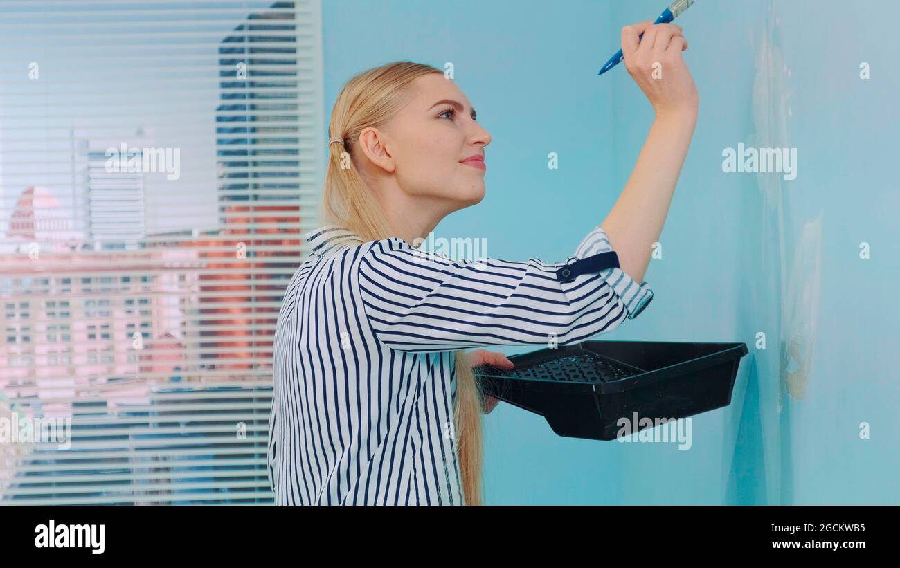 Nahaufnahme einer Frau, die in einem Hausraum eine Blume an einer blauen Wand zieht. Im Hintergrund stehen am Tag Wolkenkratzer. Stockfoto