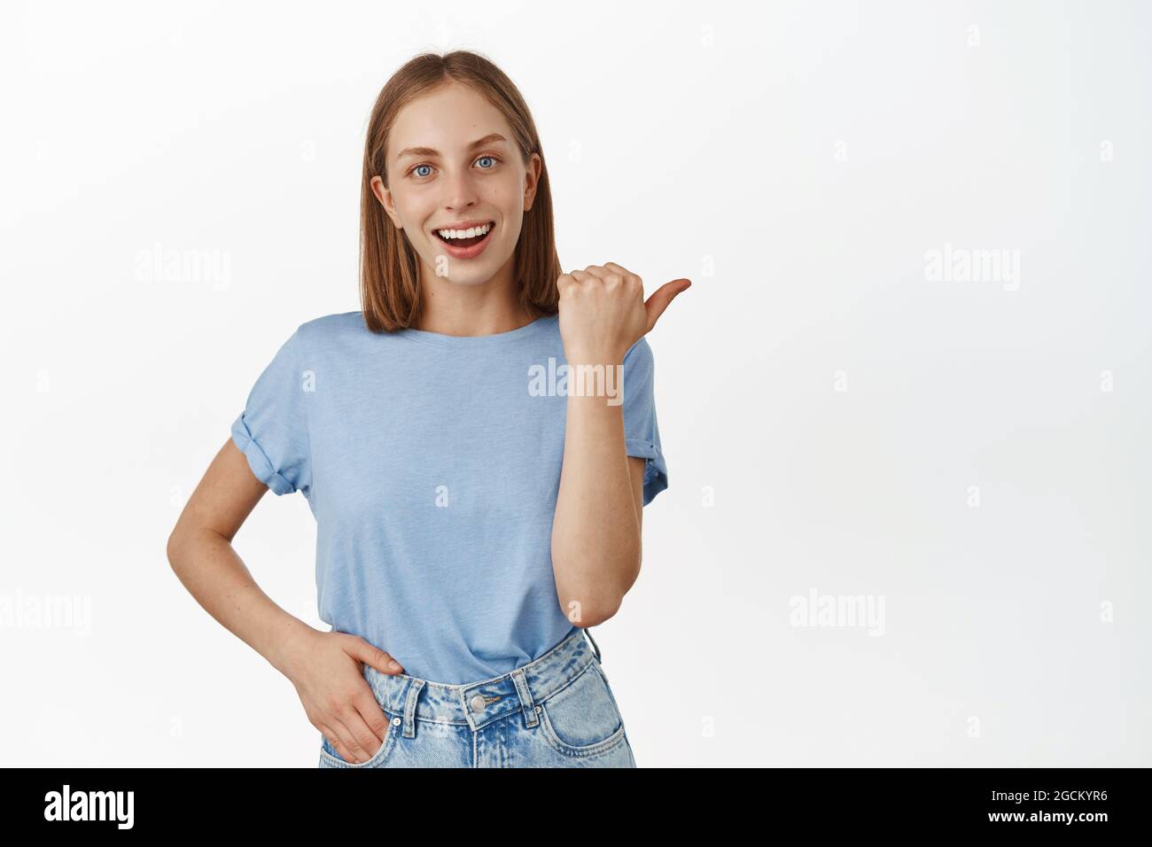 Fröhliches blondes Mädchen lacht glücklich, zeigt mit dem Finger nach rechts, zeigt Logo oder Verkauf adveorful, empfehlen Geschäft, Shop-Link, steht gegen weiß Stockfoto