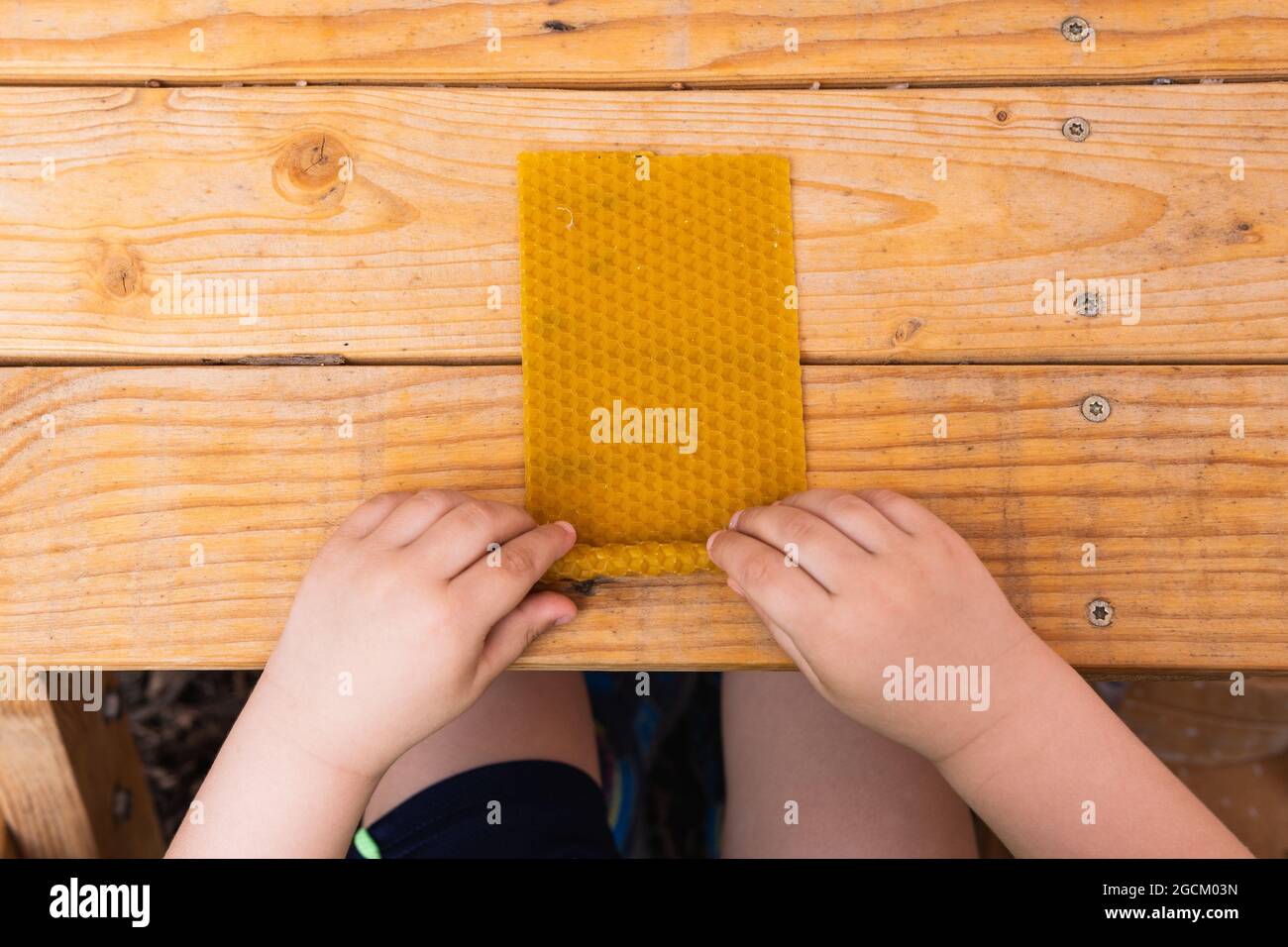 Draufsicht auf die Ernte anonymes Kind rollt Bienenwachs und macht Kerze am Holztisch Stockfoto