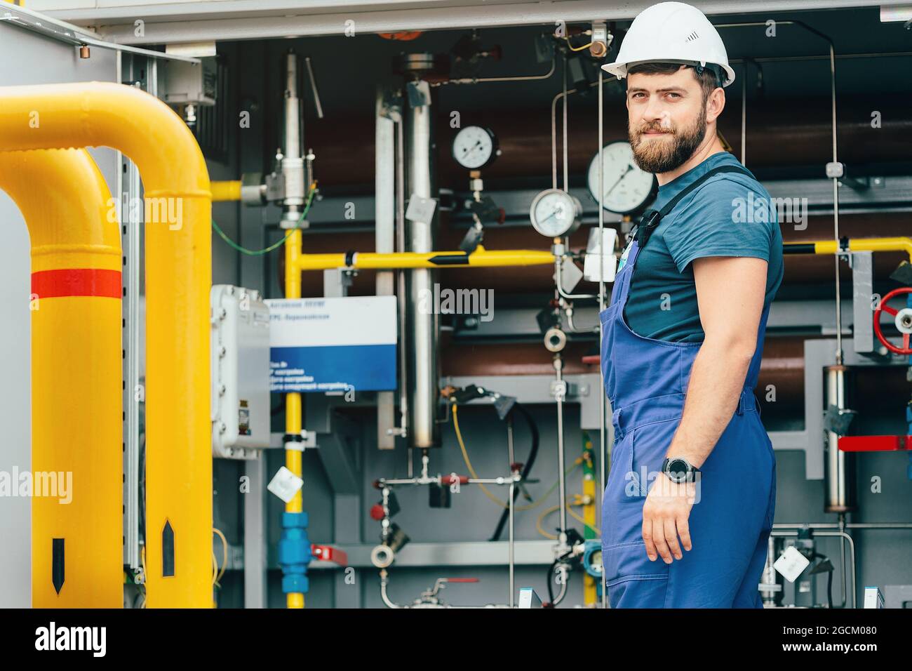 Porträt eines Gasarbeiters in einem Helm und einem Arbeitsüberfall vor dem Hintergrund von Geräten mit Rohren und Manometern. Gasodoriereinheit. Betreiber der Gasverteilerstation. Stockfoto