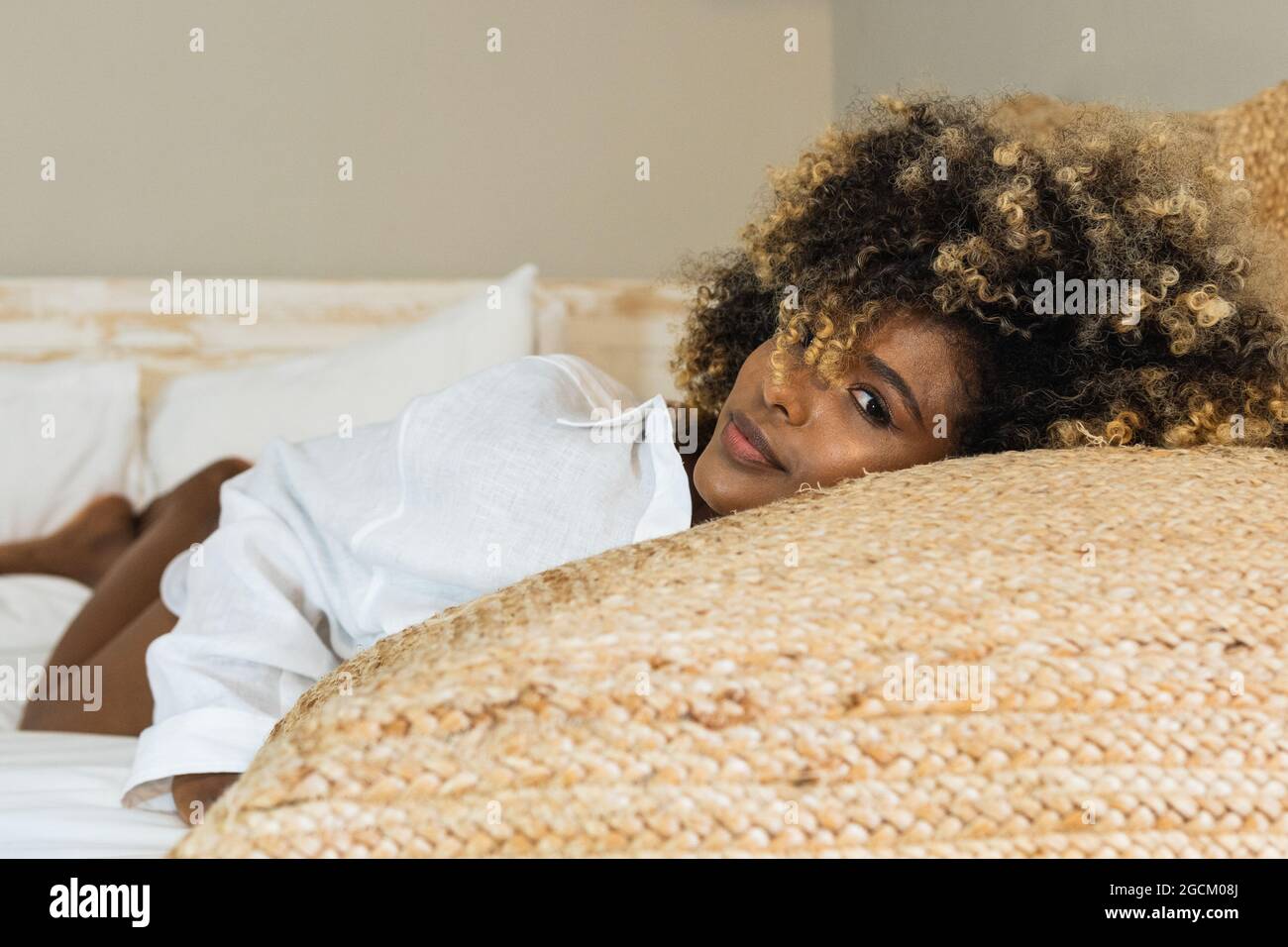 Attraktive afroamerikanische Frau, die sich auf dem Bett niederlegt und die Kamera anschaut Stockfoto