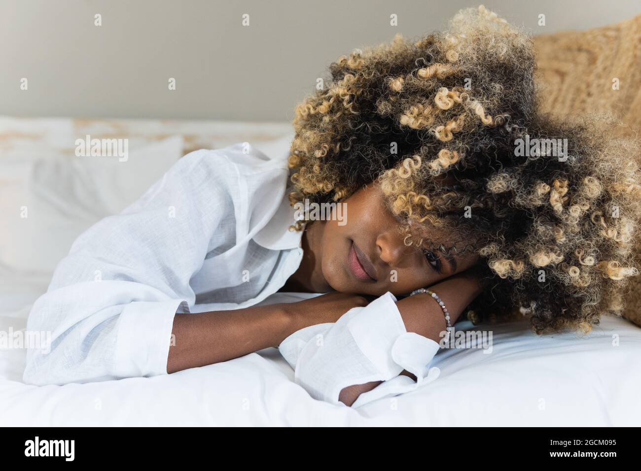 Attraktive afroamerikanische Frau, die sich auf dem Bett niederlegt und die Kamera anschaut Stockfoto