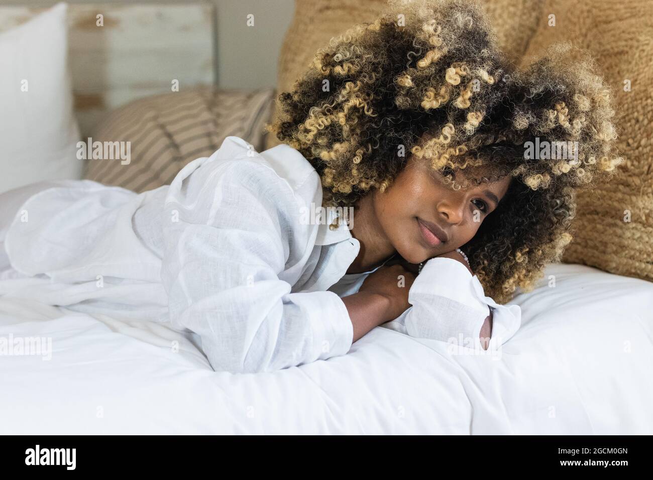 Attraktive afroamerikanische Frau, die sich auf dem Bett niederlegt und die Kamera anschaut Stockfoto