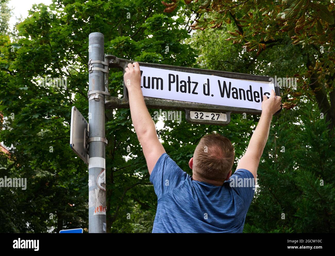 Berlin, Deutschland. August 2021. Alexander Freier-Winterwerb (M), SPD-Kandidat für das Repräsentantenhaus der Bezirke Alt-Treptow, Plänterwald und Baumschulenweg, legt vor der Botschaft von Belarus ein Straßenschild mit der Aufschrift „zum Platz des Wandels“ auf. Symbolisch zum Jahrestag der umstrittenen Präsidentschaftswahl in Belarus benennen er und sein Parteikollege Trasnea die Straße "am Treptower Park" "zum Platz des Wandels" um. Quelle: Annette Riedl/dpa/Alamy Live News Stockfoto