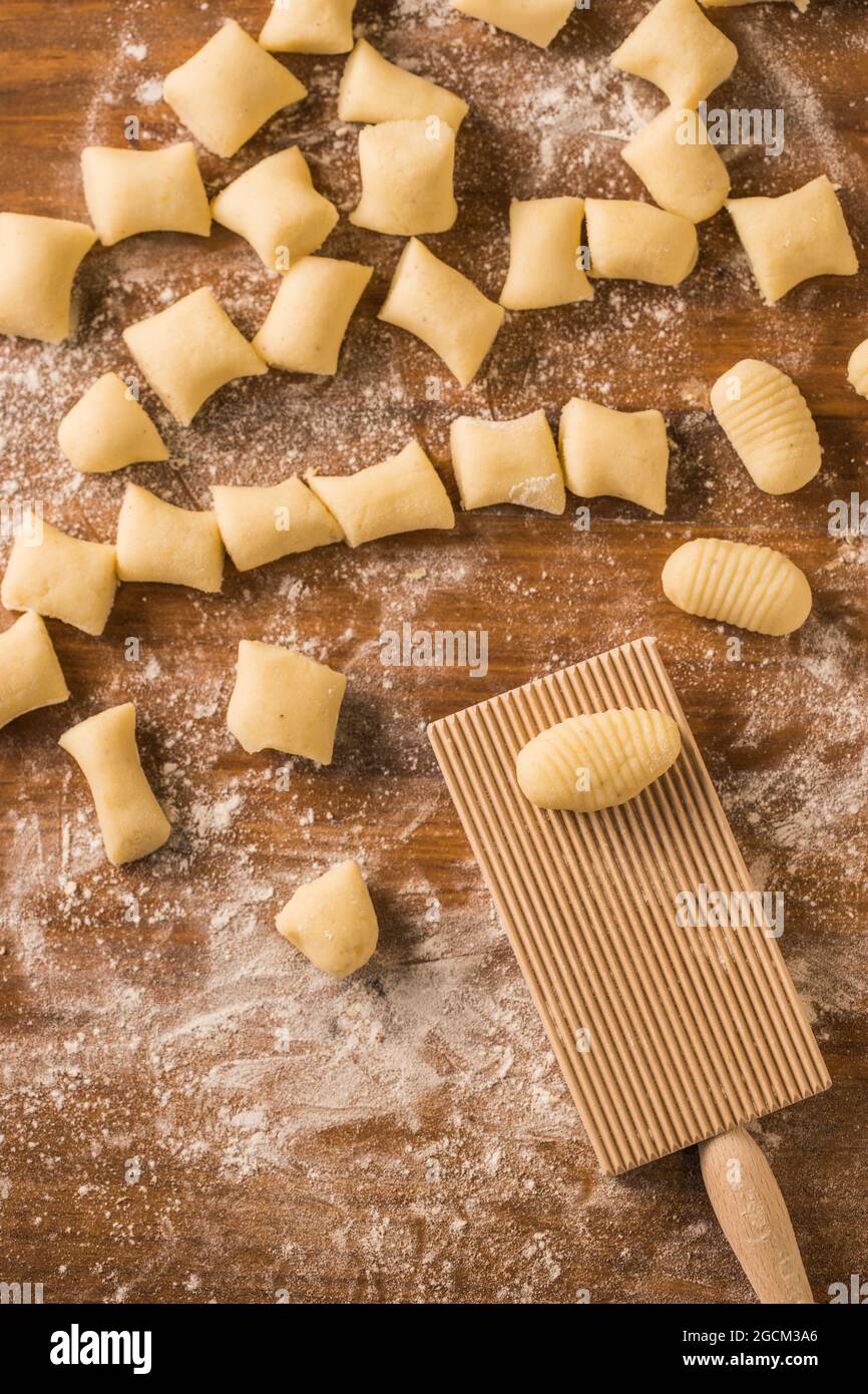 Draufsicht auf weiche rohe Teigstücke, die während der Gnocchi-Zubereitung in der Küche auf einen mit Mehl bedeckten Holztisch in der Nähe des Rippenbretts gelegt werden Stockfoto