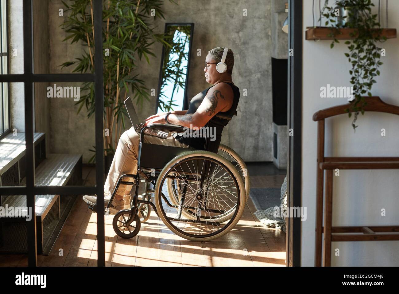 Seitenansicht Porträt einer zeitgenössischen tätowierten Frau mit Behinderung, die Musik hört, während sie sich zu Hause entspannt Stockfoto