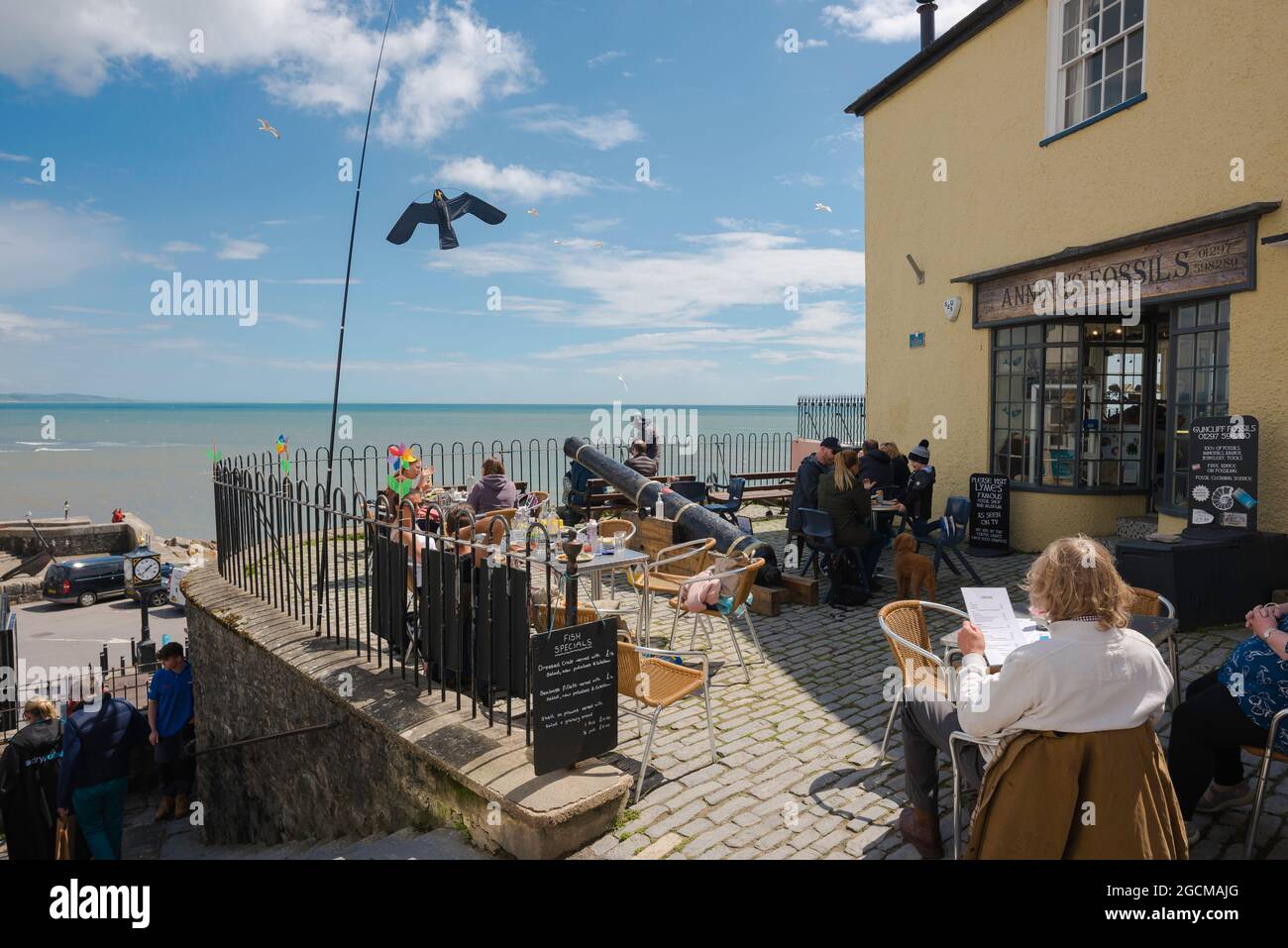 Dorset Coast, Blick auf Menschen entspannen auf einer Café-Terrasse mit Blick auf die Küste in Lyme Regis, Dorset, England, Großbritannien Stockfoto