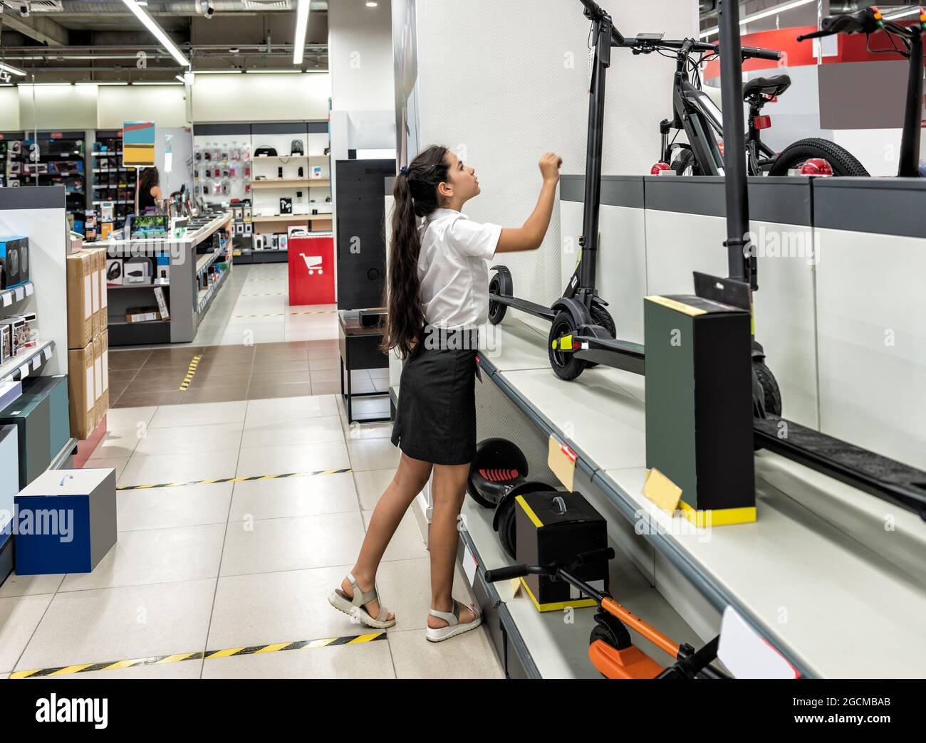 Ein Teenager-Mädchen in einem Geschäft untersucht einen Elektroroller Stockfoto