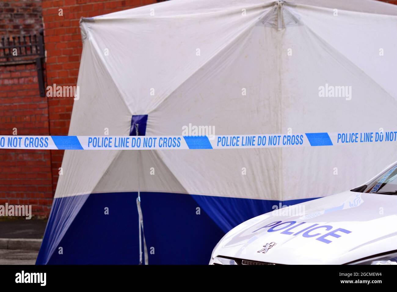 Polizeilinie oder Absperrung: „nicht überqueren“ und forensisches Zelt und Vorderseite des Polizeiautos in Manchester, England, Großbritannien Stockfoto