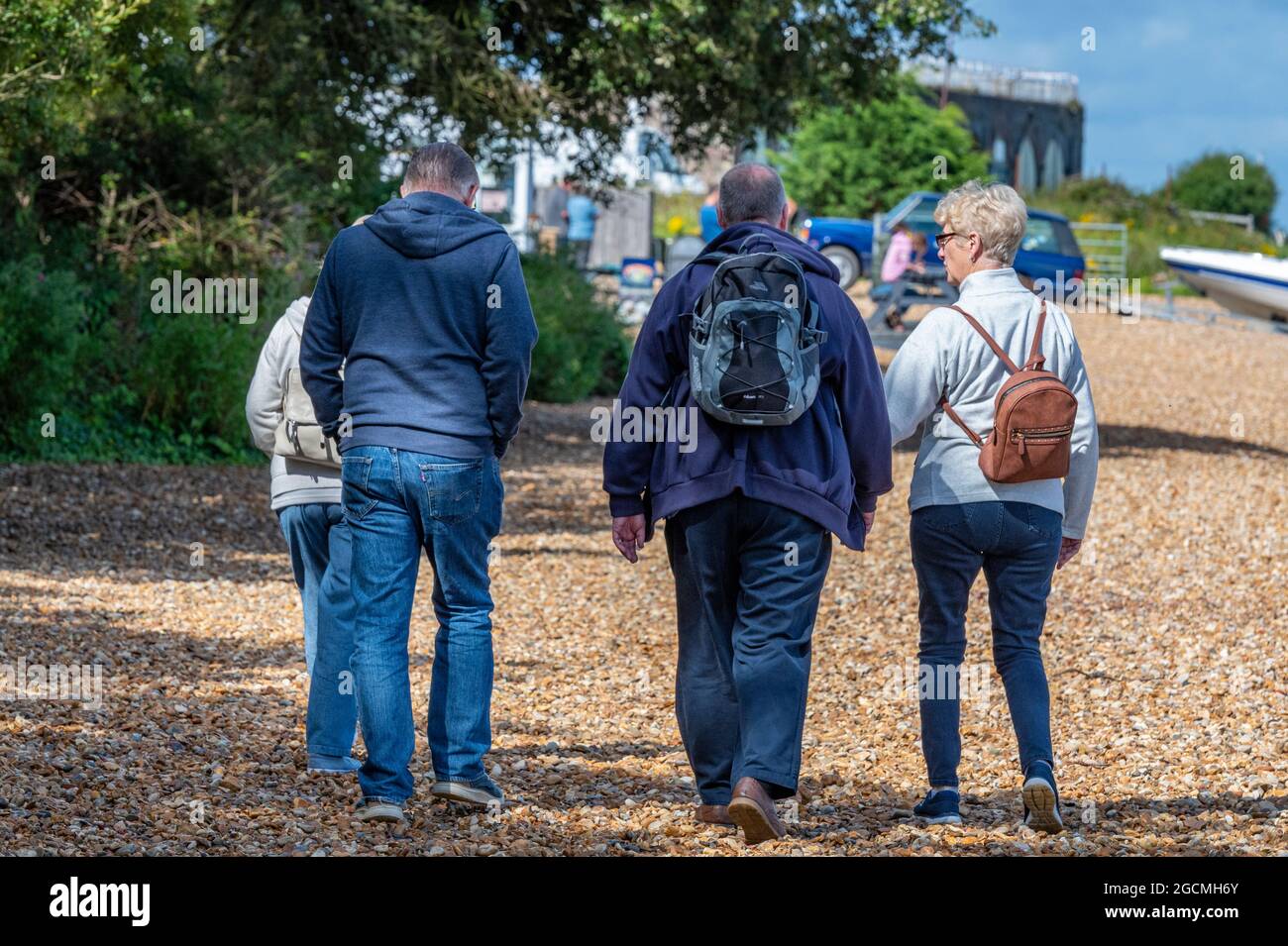 Vier Freunde mittleren Alters, die gemeinsam am Strand auf der Insel wight uk Urlaub machen. Freunde, die gemeinsam am Meer spazieren. Kiesstrand. Stockfoto