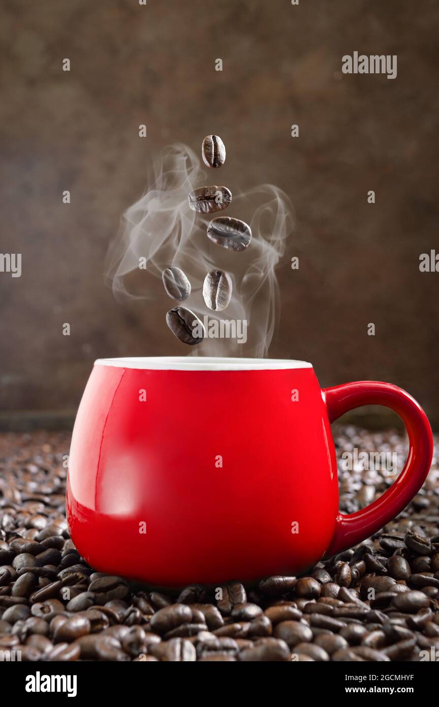 Geröstete Kaffeebohnen fallen in eine rote Tasse heißen Espresso. Das Konzept eines morgendlichen Auflassens von Heiterkeit und Energie. Vertikale Ansicht Stockfoto