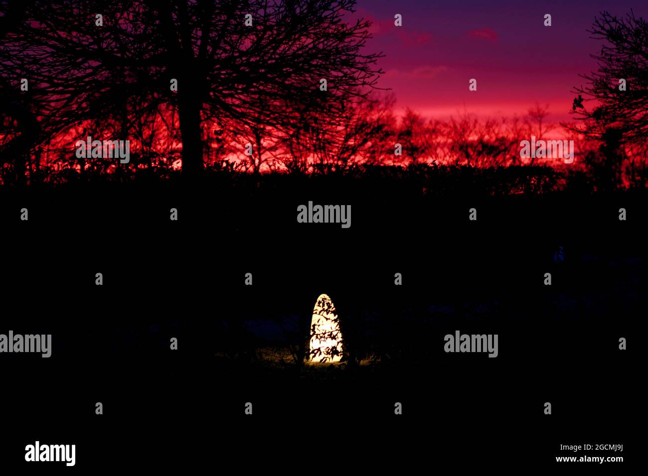 Nachtlichter im Park. Stimmungsvolle Lichtdeko im Garten mit Sonnenuntergang am Himmel. Laterne leuchtet in der Nacht. Atmosphärische Stimmung der goldenen Stunde. Stockfoto