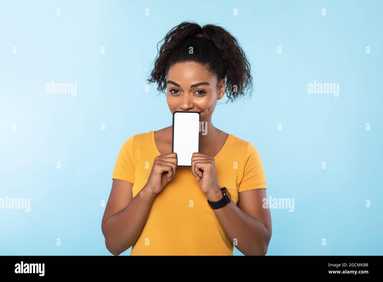 Afro-Frau mit Handy und Mockup-Platz neben ihrem Gesicht auf blauem Hintergrund. Neue tolle mobile App, Website Stockfoto
