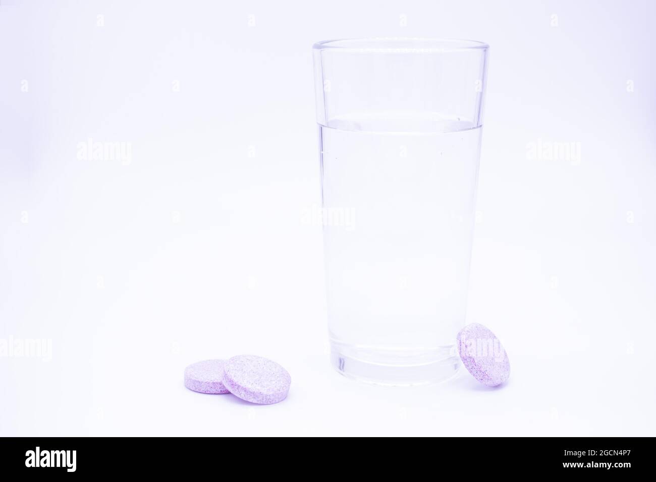 Transparentes Glas mit sauberem Wasser, daneben löslich. rosa Tabletten Vitamin C, Nahrungsergänzungsmittel, Schmerzmittel sofort oder auflösen. Stockfoto
