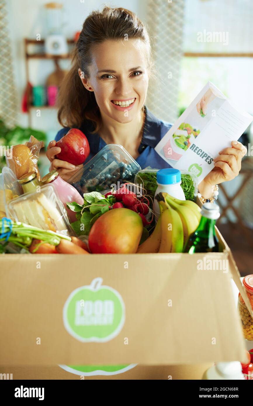 Lieferung von Lebensmitteln. Glückliche Frau mittleren Alters mit Food-Box und Rezepte Liste in der Küche. Stockfoto