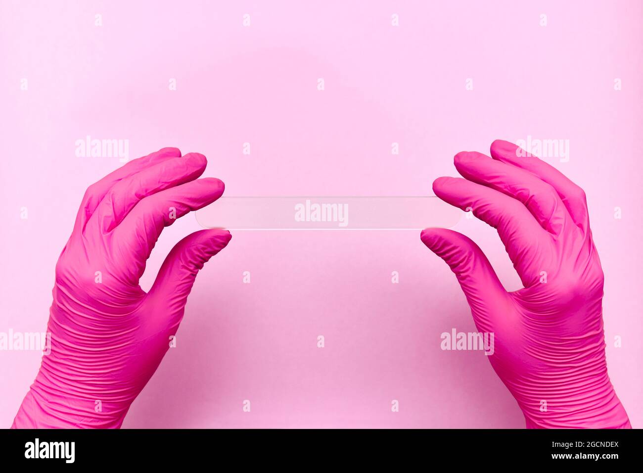 Medizinischer Spatel horizontal in zwei Händen in Schutzhandschuhen. In rosa Tönen. Stockfoto