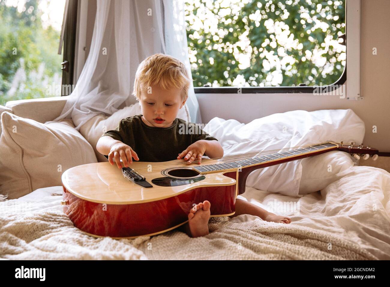 Niedlicher Junge spielen Gitarre sitzen auf dem Bett im Anhänger rv. Liebenswert kleines Kind unterhalten Reisen auf Wohnmobil Stockfoto