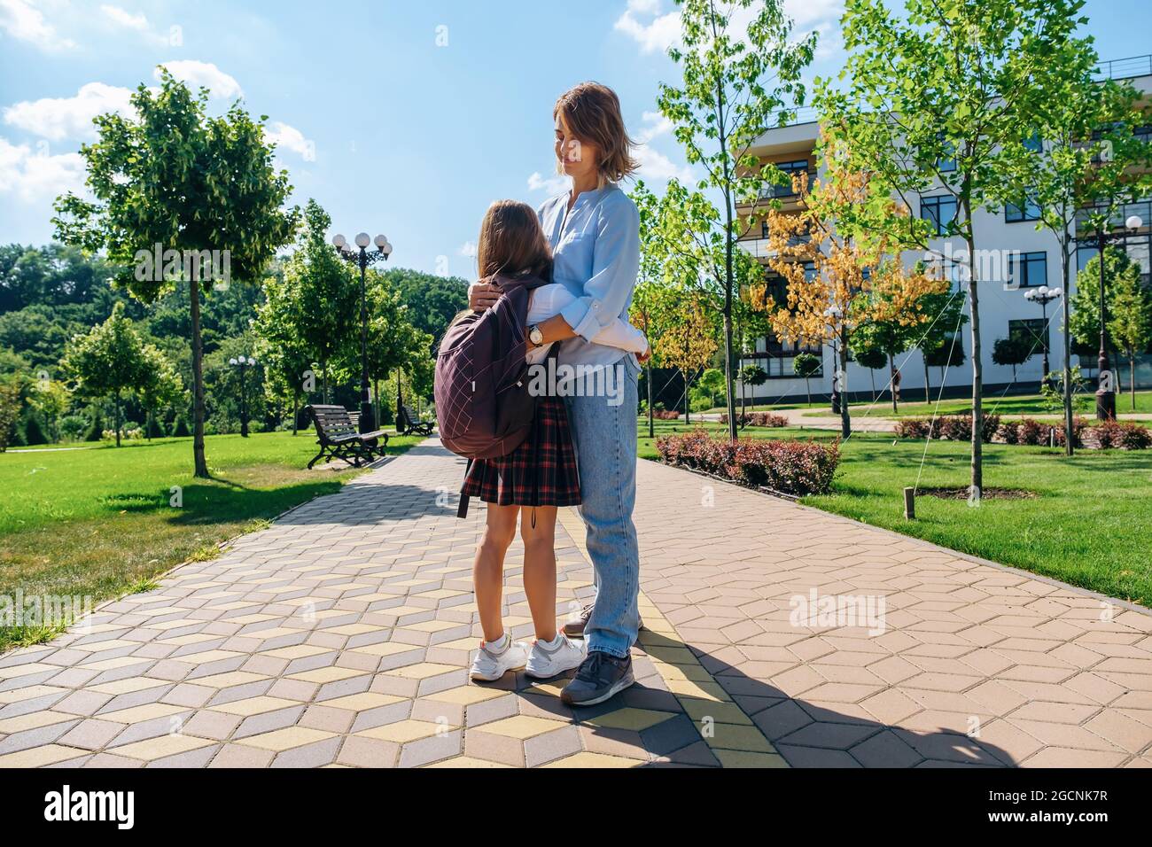 Schülerin mit Rucksack und Uniform umarmt ihre Mutter, bevor sie zur Schule geht. Stockfoto