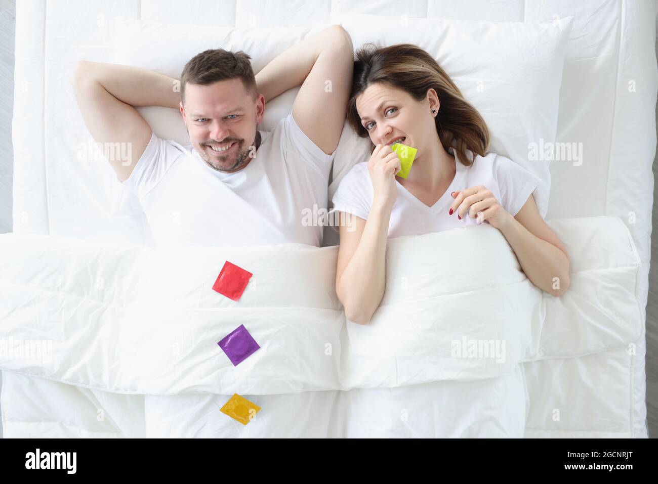 Glücklicher Mann Frau liegt auf dem Bett mit Kondomen Stockfoto