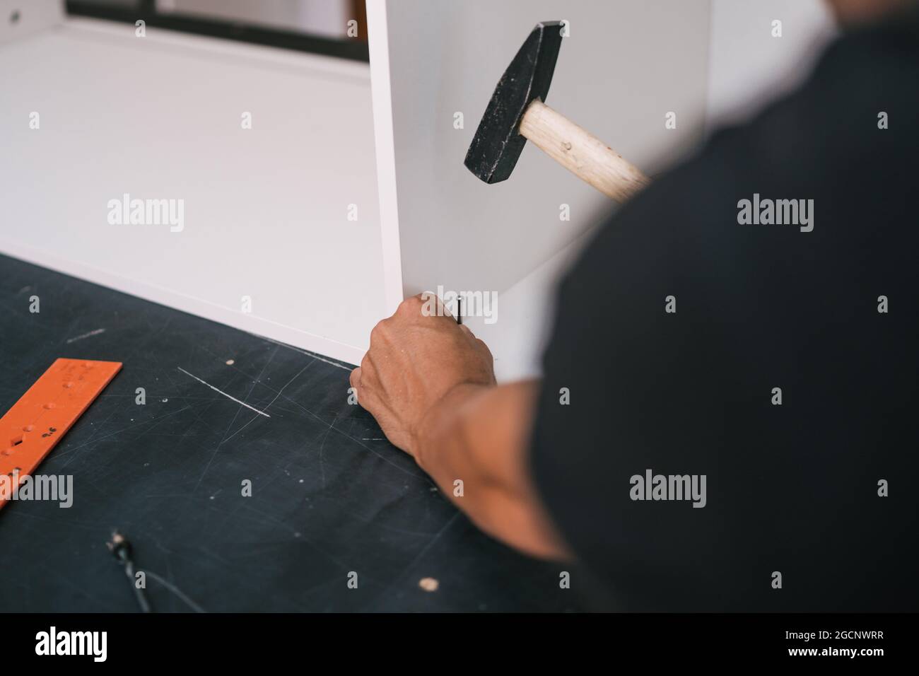 Hände nageln eine Schraube mit einem Hammer in ein weißes Holzmöbel Stockfoto