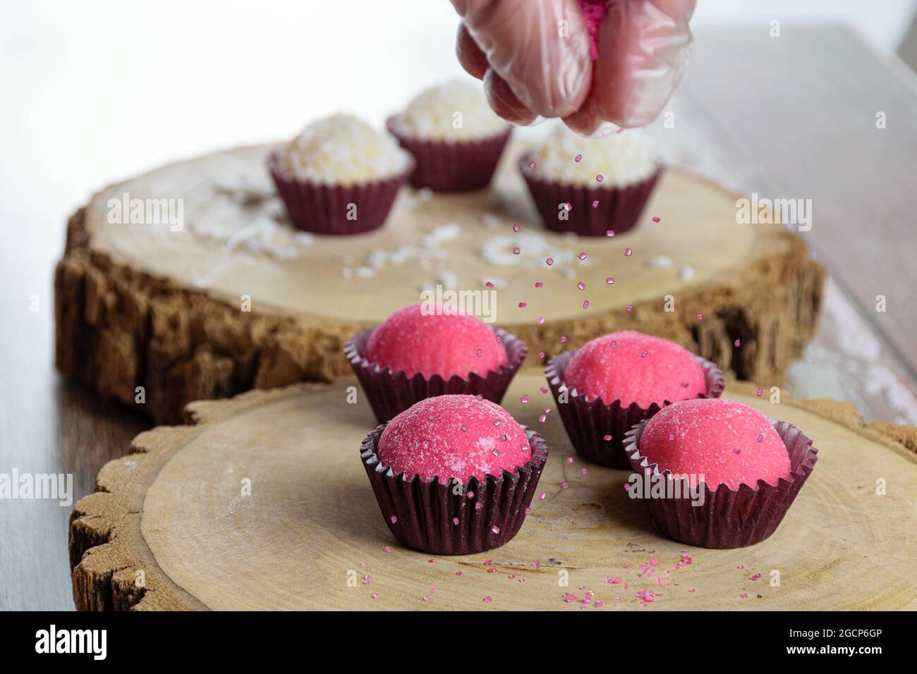 Erdbeer-Brigadeiros (Bicho de PE) auf Baumstammschalen. Konditor setzt rosa Kristallzucker darauf. Stockfoto