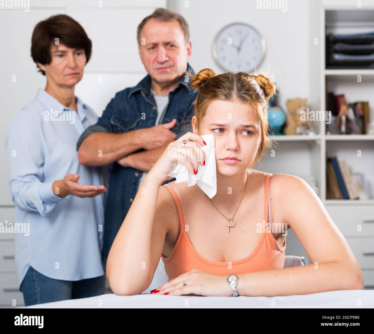 Die Eltern sympathieren mit ihrer traurigen Tochter, die am Tisch sitzt Stockfoto