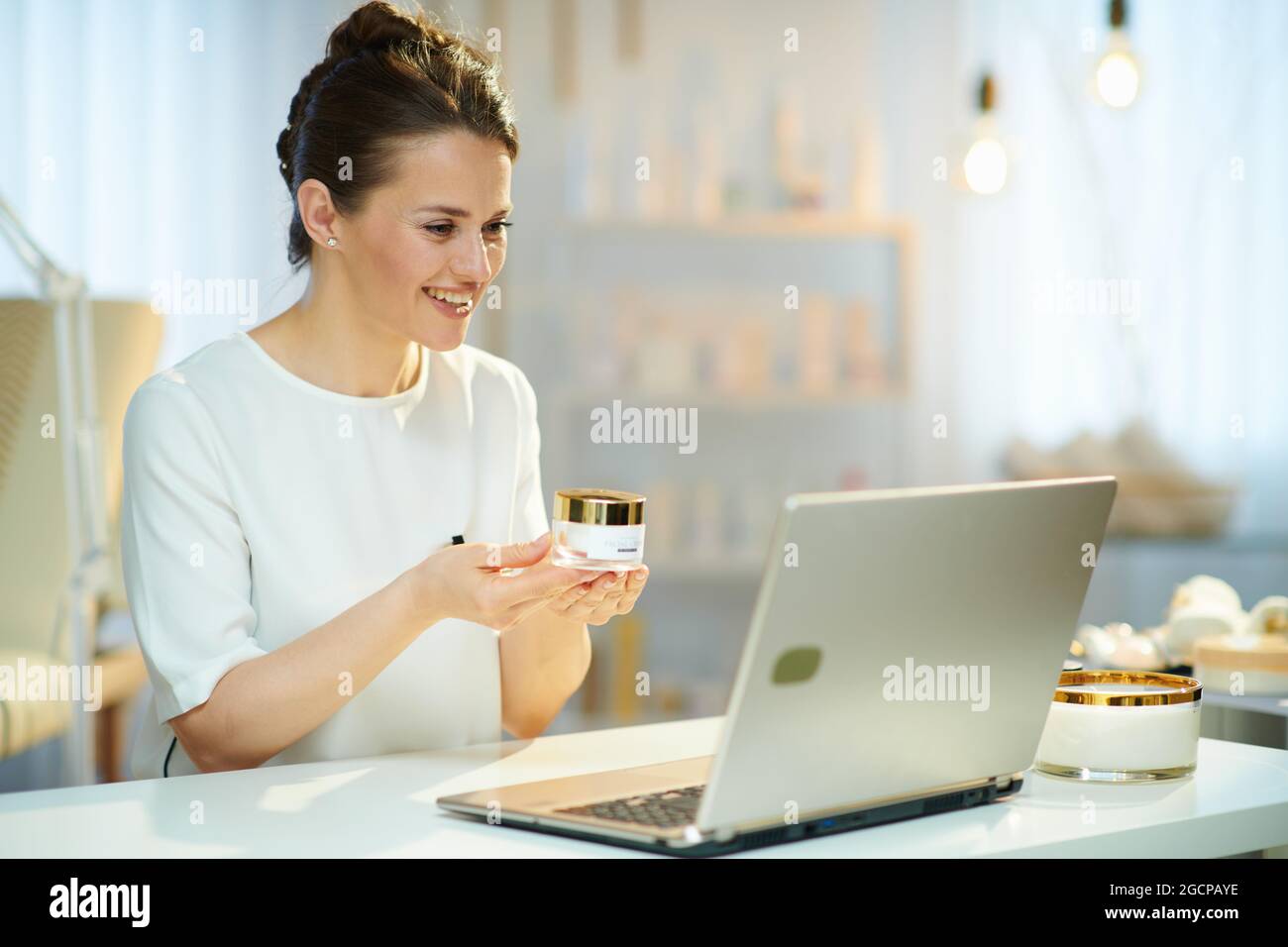 Lächelnde Angestellte im mittleren Alter mit Laptop, die im modernen Schönheitssalonstudio einen Videochat führt. Stockfoto