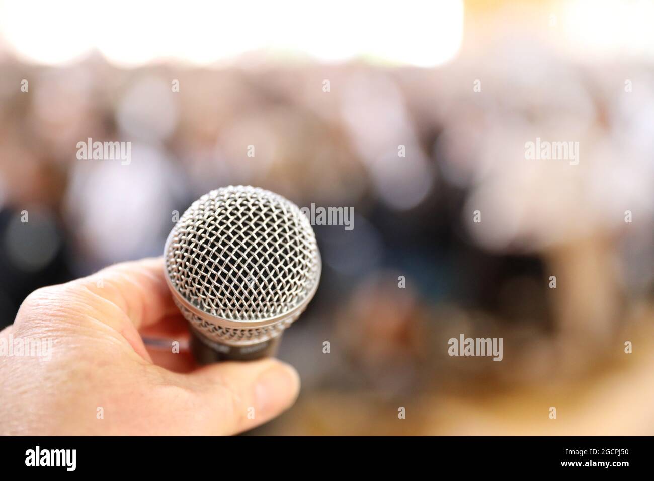 Ein Mikrofon ganz in der Nähe mit einer Hand, um es in Vorbereitung auf das Sprechen mit einem großen Publikum zu schließen. Angst vor dem Konzept des öffentlichen Sprechens. Stockfoto