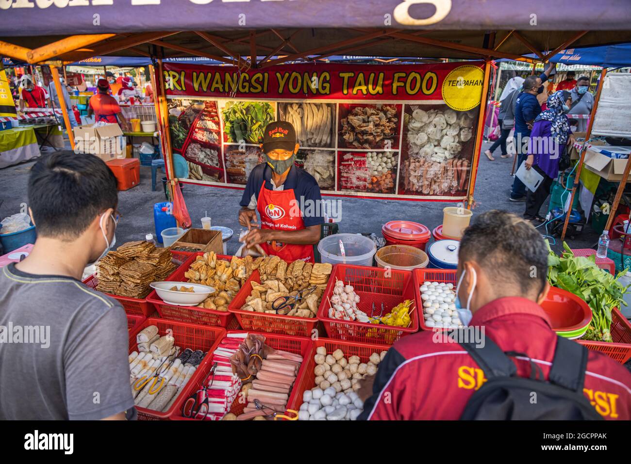 Ein Tofu-Verkäufer auf dem Markt Putrajaya, Kuala Lumpur. Die Kunden warten darauf, dass der Verkäufer ihre Waren einpackt. Mann mit Gesichtsmaske verkauft Tofu Stockfoto