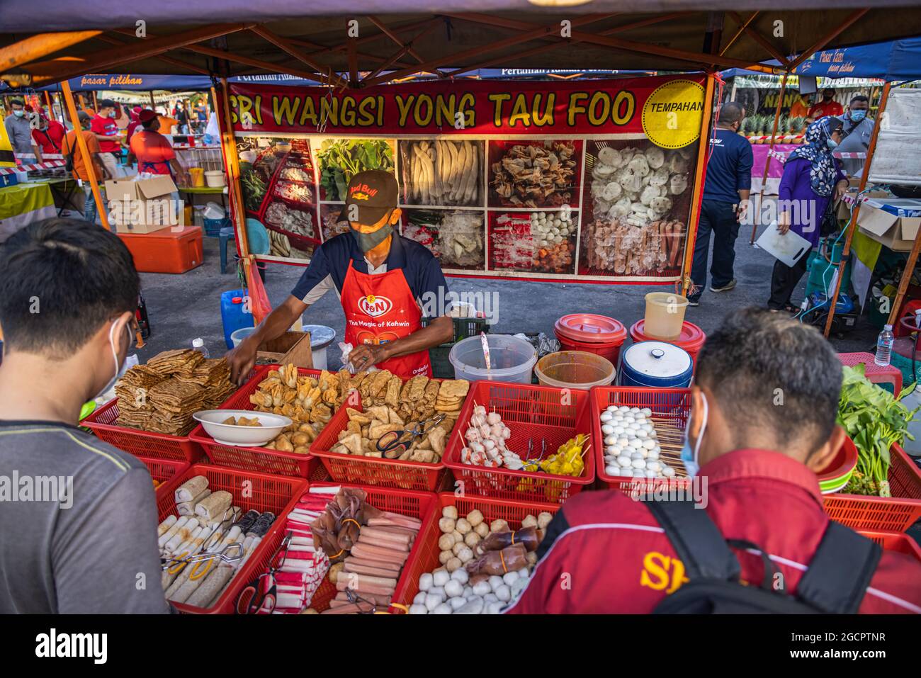 Ein Tofu-Verkäufer auf dem Markt Putrajaya, Kuala Lumpur. Die Kunden warten darauf, dass der Verkäufer ihre Waren einpackt. Mann mit Gesichtsmaske verkauft Tofu Stockfoto