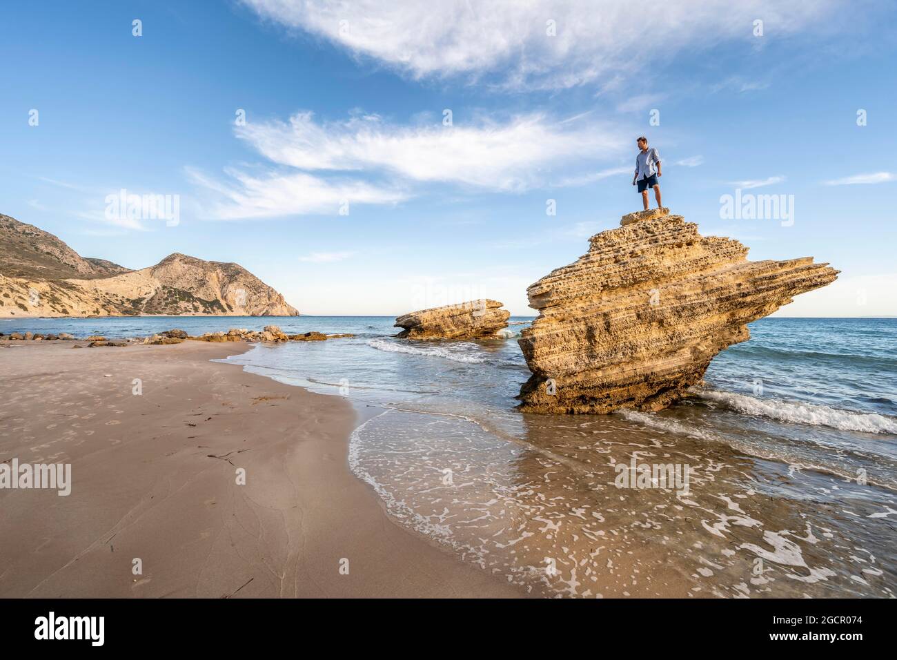 Junger Mann, der auf einem Felsen steht, Felsen im Wasser, Sandstrand mit felsigen Klippen, Paralia Paradisos, Kos, Dodekanes, Griechenland Stockfoto