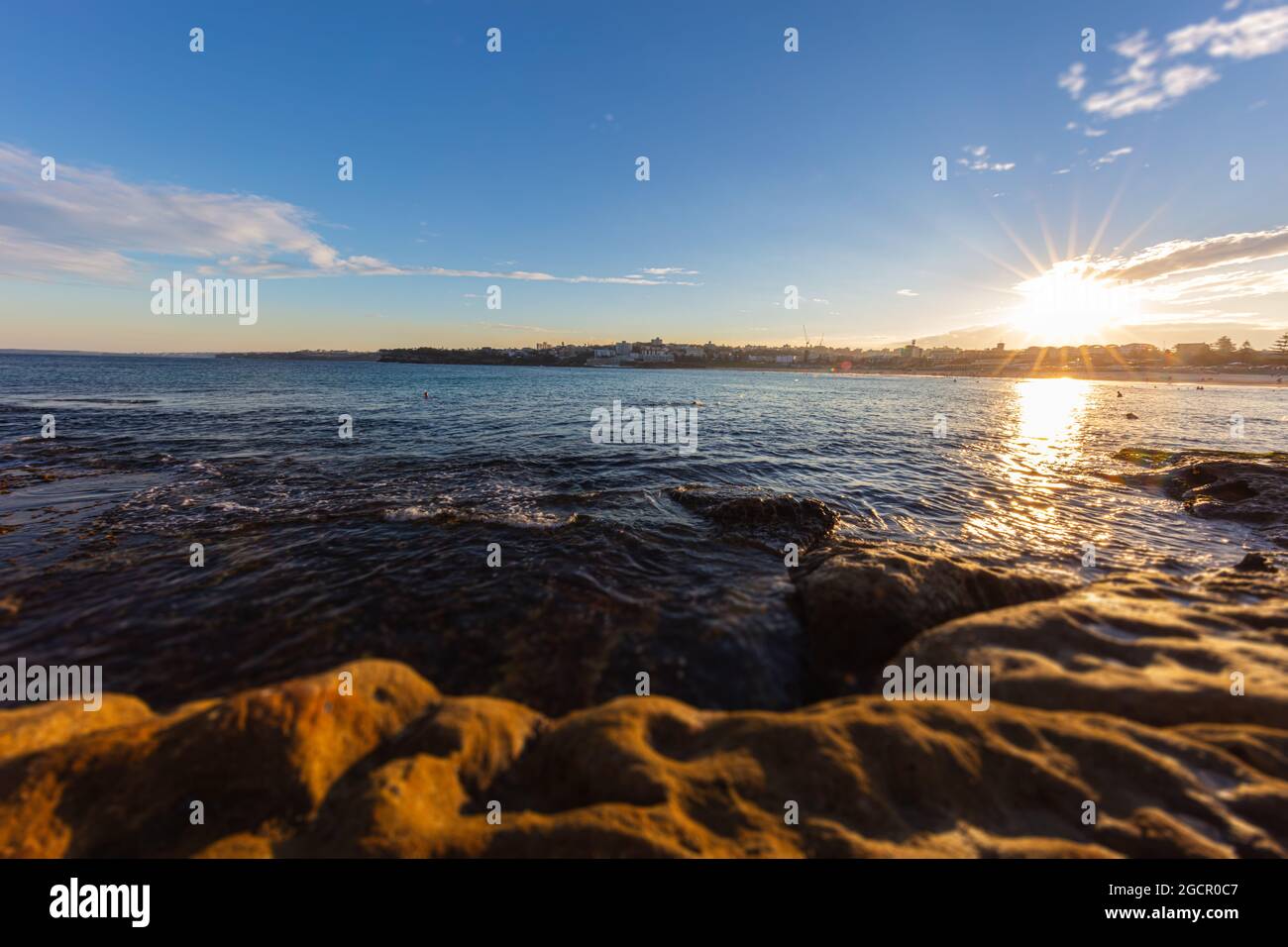 Felsige Küste rund um Bondi Beach, Sydney, Australien. Sonnenuntergang in der Nähe des berühmten Surfer-Strandes. Sonnenuntergang über dem pazifik. Die Sonne spiegelt sich im Smoot Stockfoto