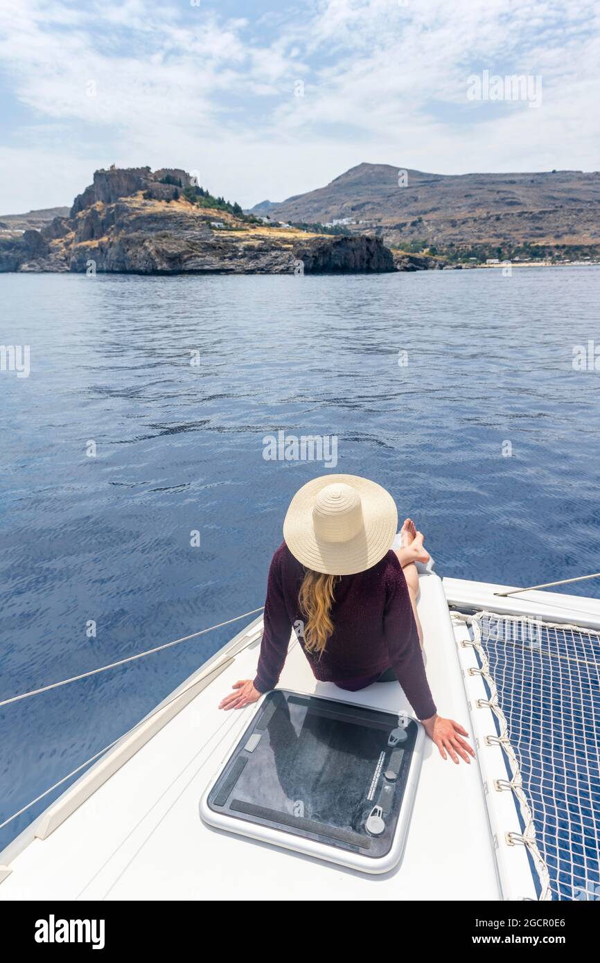 Junge Frau mit Sonnenhut, die auf einem Boot sitzt, Lindos, Rhodos, Dodekanes, Griechenland Stockfoto