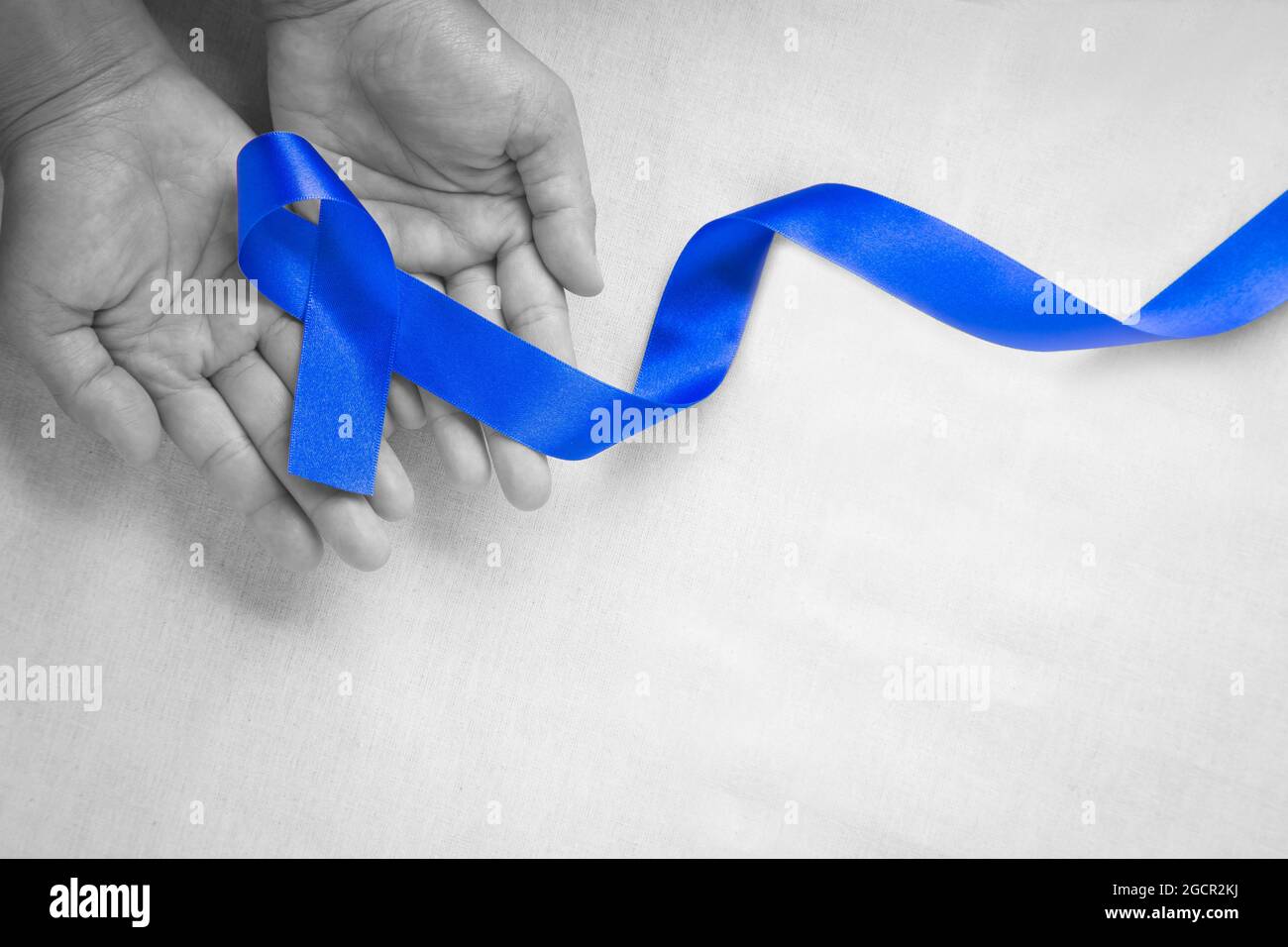 Hände mit tiefblauem Band auf weißem Stoff mit Kopierraum. Darmkrebs Bewusstsein, Colon Krebs der älteren Person und Welt Diabetes Tag, Chil Stockfoto