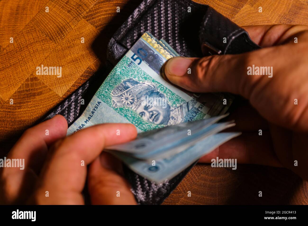 Männliche Hände zählen 50 Ringgit Malaysia in einer Ledertasche auf einem Holztisch. RM50 in Mans Hand. Malaysischer Ringgit, der von einem jungen Mann in einer Brieftasche gezeigt wird. Cl Stockfoto