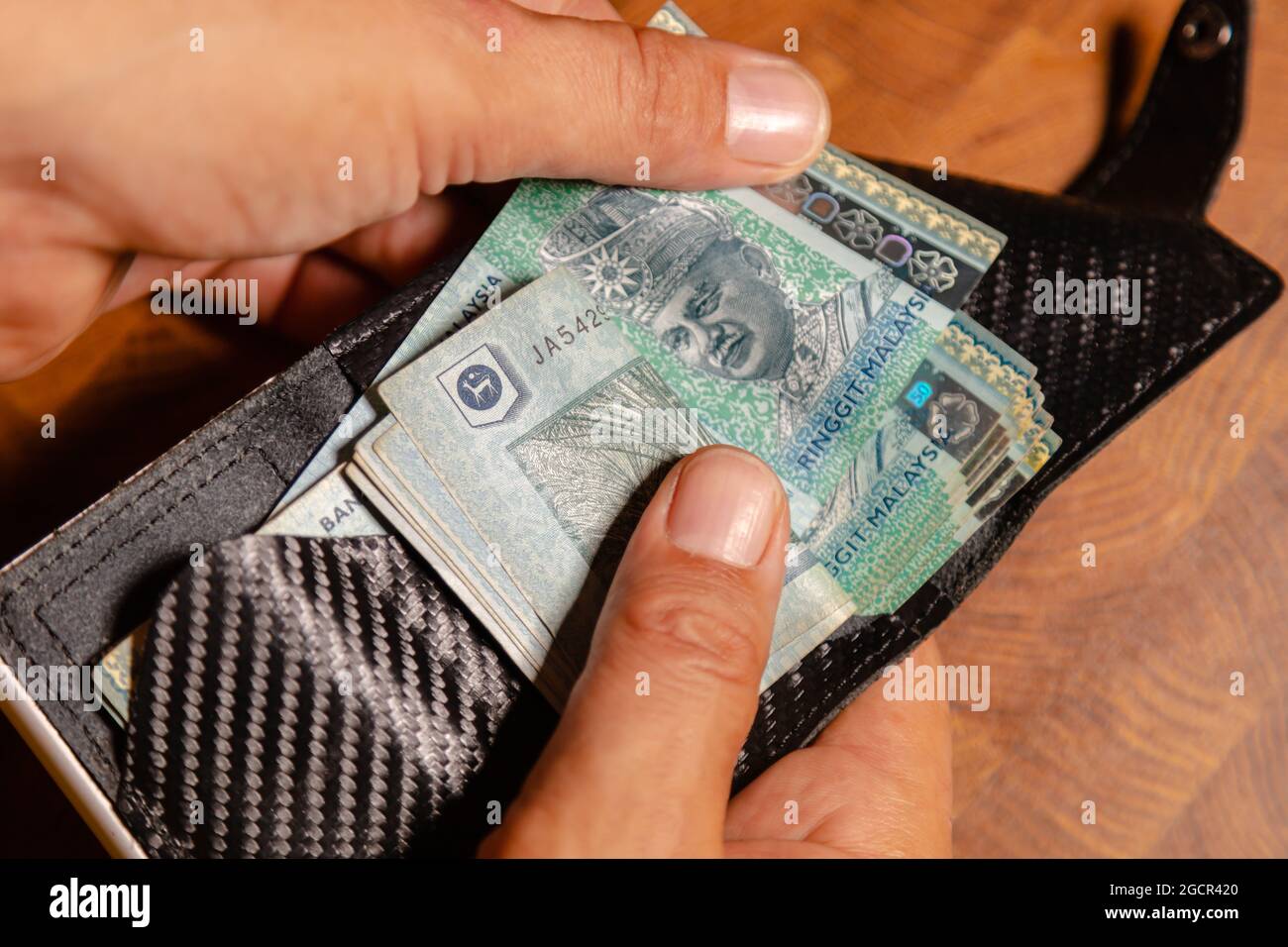 Männliche Hände zählen 50 Ringgit Malaysia in einer Ledertasche auf einem Holztisch. RM50 in Mans Hand. Malaysischer Ringgit, der von einem jungen Mann in einer Brieftasche gezeigt wird. Cl Stockfoto