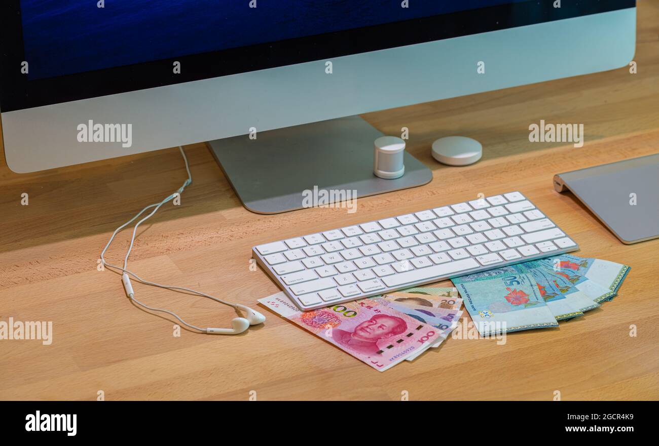 Chinesische und malaysische Währung unter einer Aluminium-Computertastatur auf einem Holzschreibtisch. Bund von 50 Malaysia Ringgit und China Renminbi oder Yuan Stockfoto