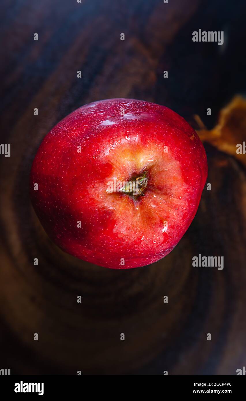 Eine Nahaufnahme eines frischen roten Apfels auf einem Holztisch. Wasser tropft auf die Oberfläche des sogenannten Weihnachtsapfels. Makrofotografie Stockfoto